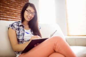 Asian woman on the couch writing her bullet journal ideas