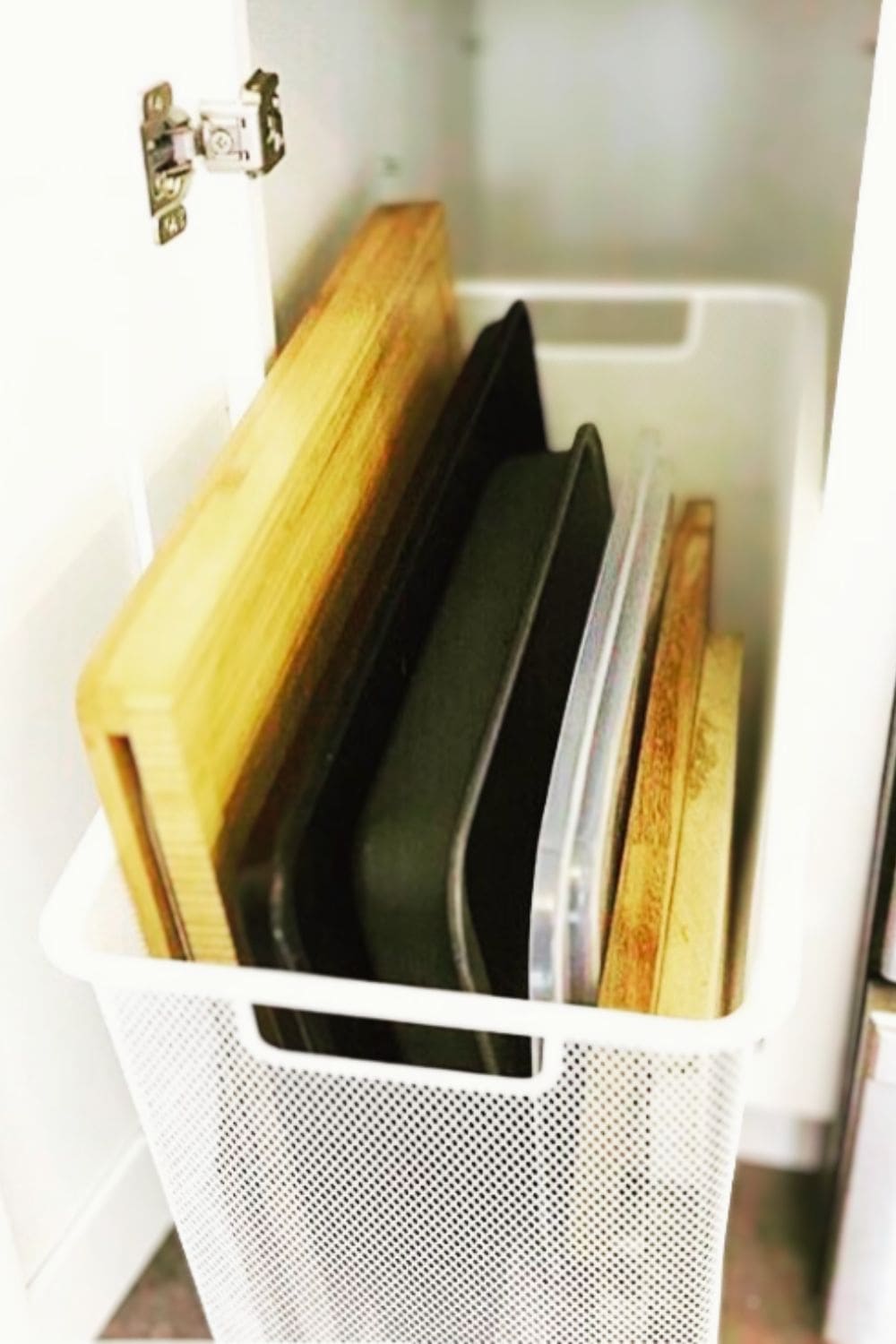 Wire bin holding cutting boards upright inside a cabinet, a simple dollar store hack that keeps kitchen storage neat and makes boards easy to grab.