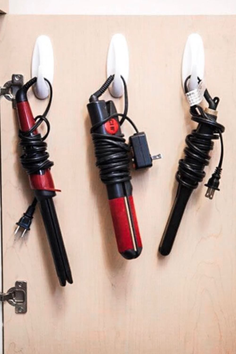 Command hooks on cabinet door with curling irons hanging on them. 