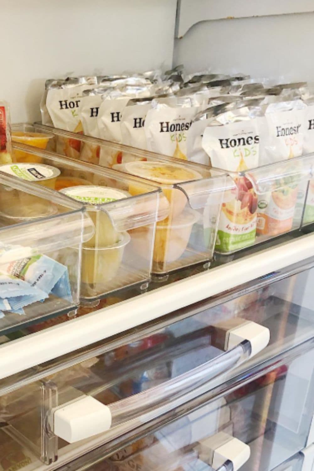 Clear bins organizing snacks inside the fridge, a practical dollar store hack that makes snack time easier for kids and keeps the fridge looking calm.