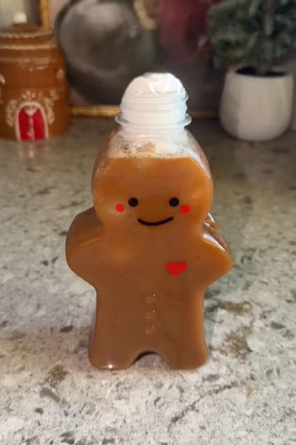 Iced coffee recipe served in a cute gingerbread-shaped bottle filled with creamy sugar-cookie flavored coffee and topped with whipped cream on a festive countertop.