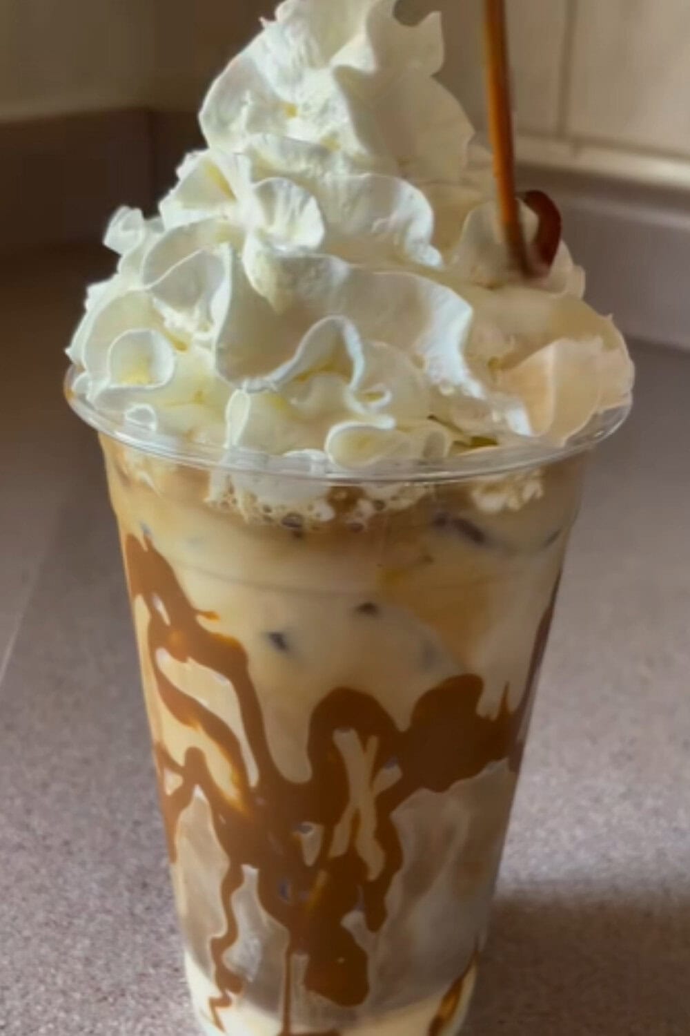 Iced coffee recipe featuring a caramel-drizzled iced coffee topped with a tall swirl of whipped cream in a clear plastic cup.