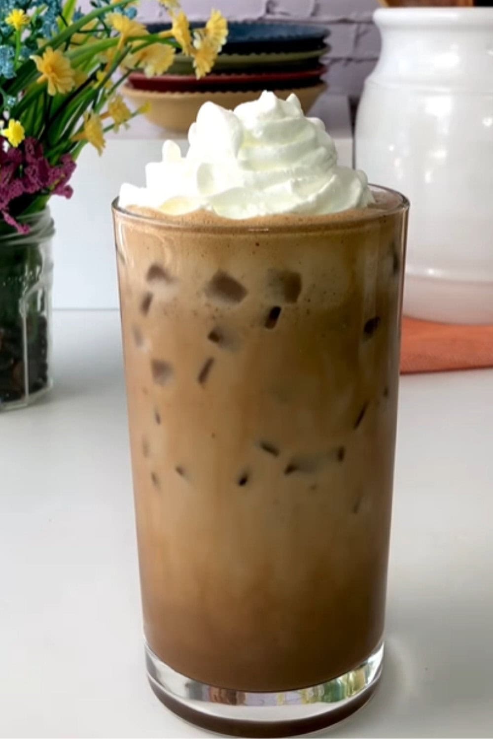 Iced coffee recipe shown as a frothy mocha-style iced coffee in a tall glass, filled with ice and topped with a generous swirl of whipped cream.