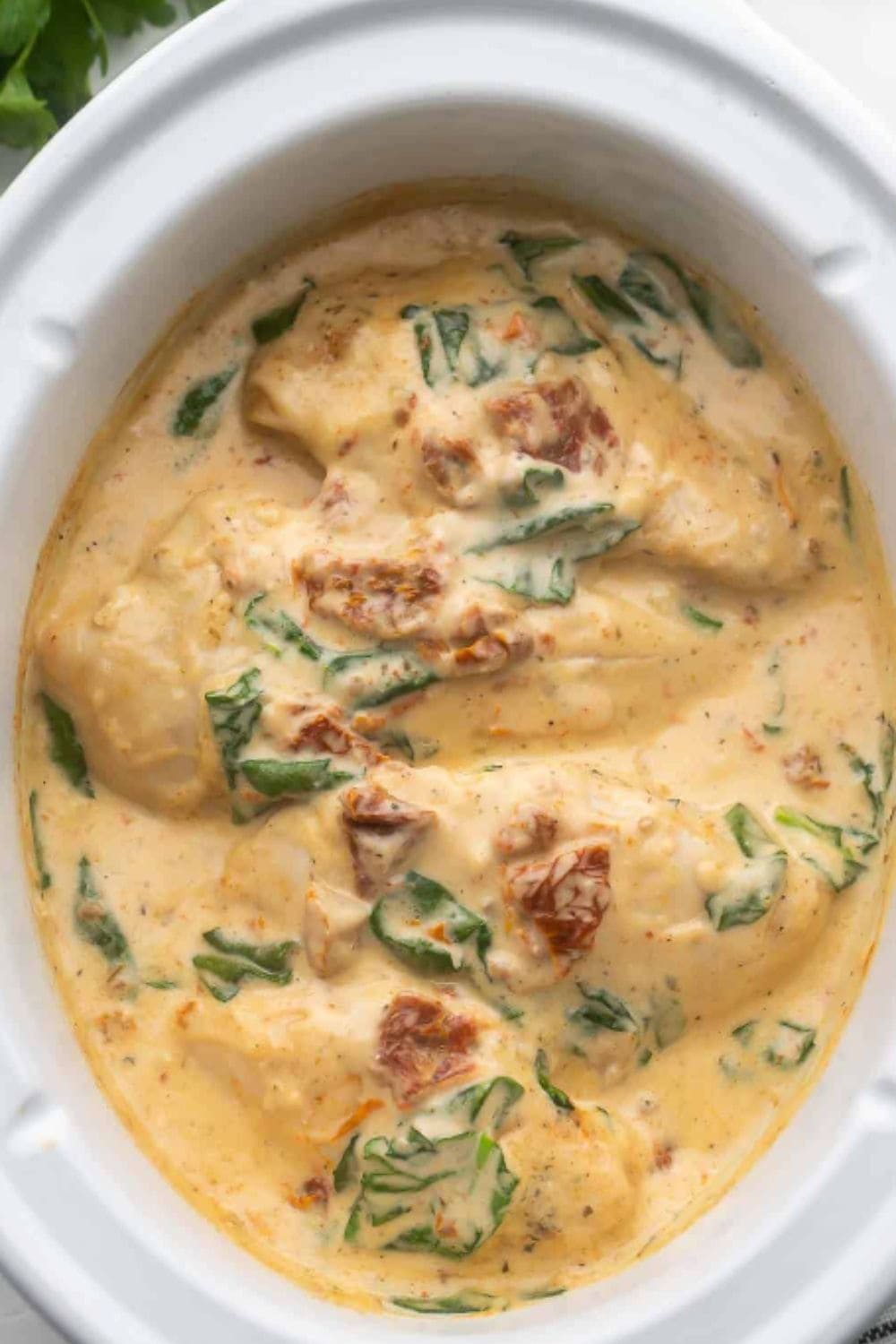Creamy Tuscan chicken simmering in the crockpot with spinach and sun-dried tomatoes, a cozy healthy dump and go crockpot dinner idea.